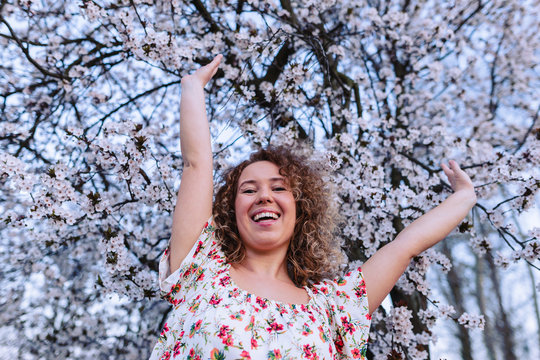 Beautiful curly woman enjoying smell flowering near the cherry tree.
