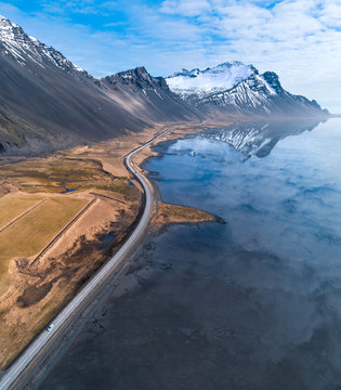 High Angle Aerial View Of A Road By Ocean Leading Towards Distance With Snow Covered Mountains In Iceland At Spring