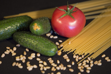 a dietary vegetarian food set of three green cucumbers, one ripe red tomato, scattered on the surface of a handful of sesame and pasta