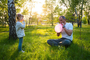 Fototapeta premium Focused father blows a balloon for his little cheerful daughter