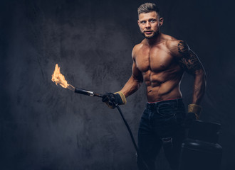 Brutal tattoed male welder with a stylish haircut and beard, with muscular body, dressed in only...