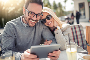 Happy couple at coffee shop looking at tablet