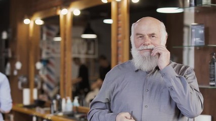 Mature man twists his mustache and posing for camera in barbershop