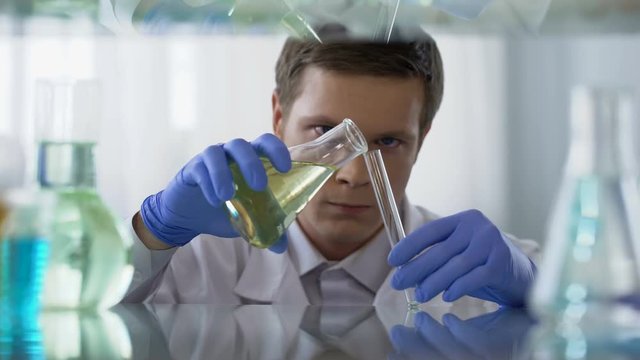 Unsure scientist pouring chemical substance into test tube, observing reaction