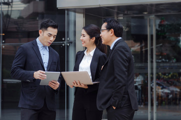 group of business people in suit talking and reading information about finance news in laptop computer together standing in modern city, network technology, internet, successful, teamwork concept