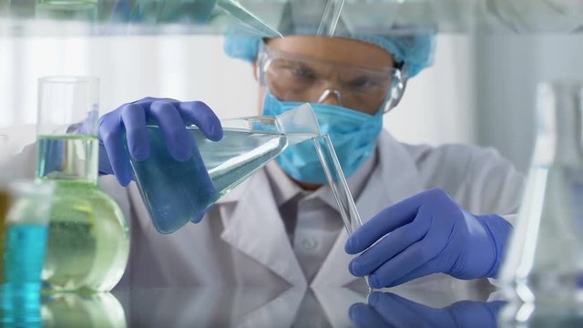 Scientist in protective goggles pouring acid liquid into vial, dangerous tests