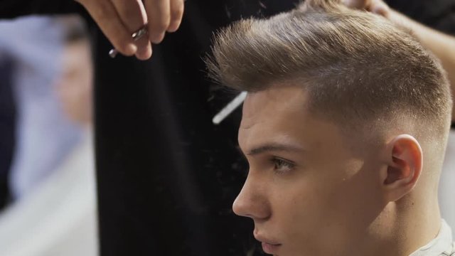 Hairstylist cuts hair of young man with scissors