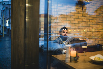 Fototapeta premium Bearded man rest in restaurant with beer glass. Beer time. serious bar customer sit in cafe drinking ale. Date meeting of hipster awaiting in pub. Businessman with long beard drink in cigar club.