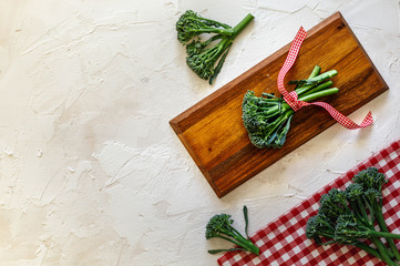 Broccolini on wooden board with red and white squares napkin on grey concret background, top view, copy space