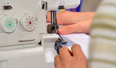 The woman at the sewing machine processes a white fabric, on manufacture close-up of a hand.