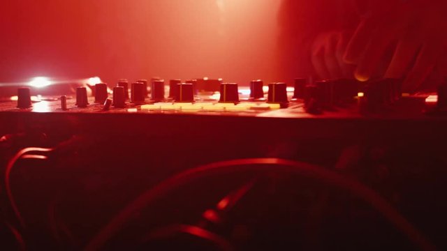 DJ plays at a concert in a nightclub, light music, smoke, back light, equipment is visible, a mixer with hands, vinyl and CD players