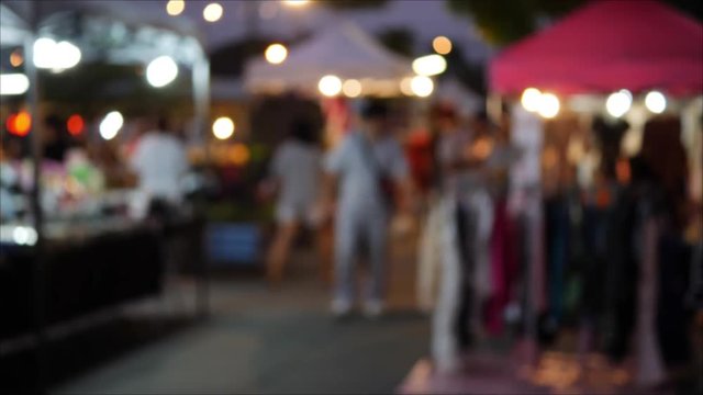 slow-motion people walking shopping in night market with booth on street, blur defocused scene