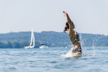 Portrait of young women jumping in Lake Constance with sailing boats in the background