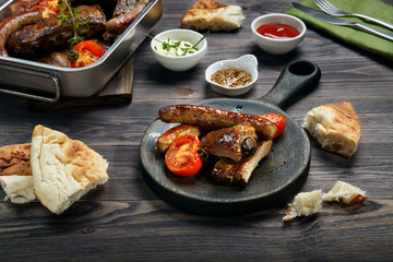 Grilled pork ribs and sausages served with tomato and sauces on wooden table.
