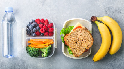 School lunch box with sandwich vegetables water almonds and fruits on grey table healthy