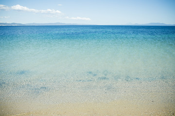 Natural beauty, sparkling, shimmering, transparent clean sea water. View on shining sea surface with waves, sand beach and skyline with mountains. Paradise concept. Place for rest and relax, resort.