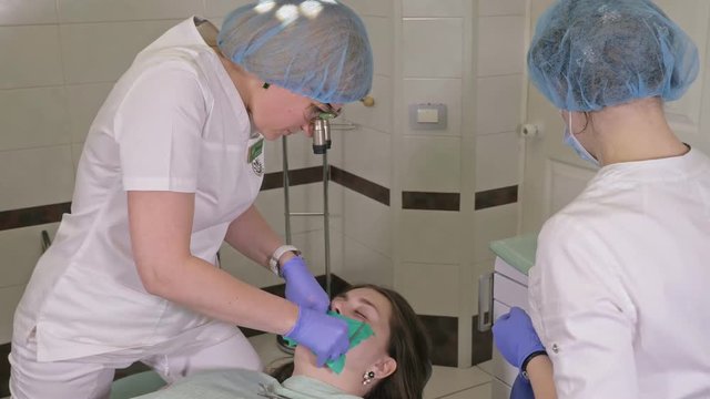Woman at dentist clinic gets dental treatment to fill a cavity in a tooth. Dental restoration and composite material polymerization with UV light and laser. Installation of dental dam.
