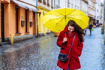 smiling woman in red coat with yellow umbrella walk by city street