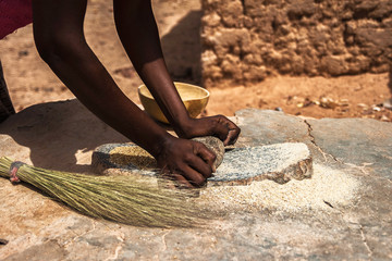 An african woman grinding cereals millet into flour using traditional grindstones, Burkina Faso.