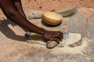 An african woman grinding cereals millet into flour using traditional grindstones, Burkina Faso.