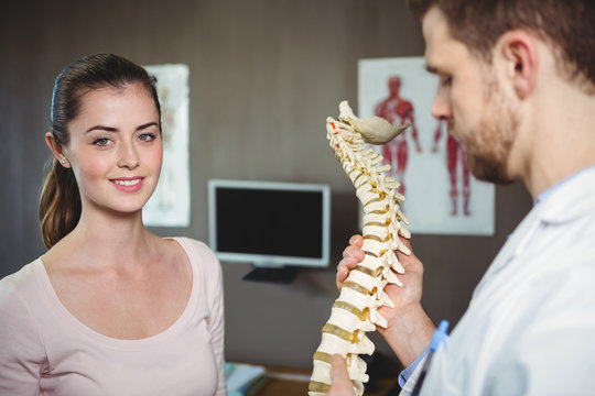 Physiotherapist holding spine model while patient smiling at camera