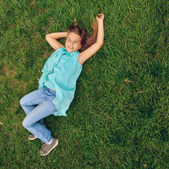 Portrait of smiling little girl lying on green grass, image with toning square aspect ratio