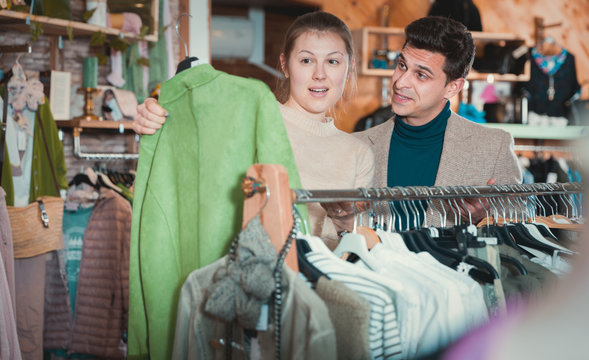 Smiling woman and man are choosing clothes and looking on green
