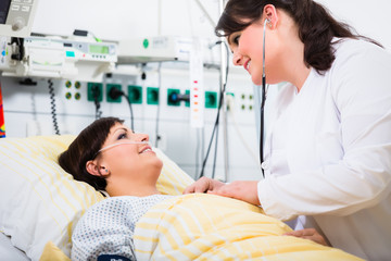 woman doctor at intensive care unit of clinic checking her patient with stethoscope