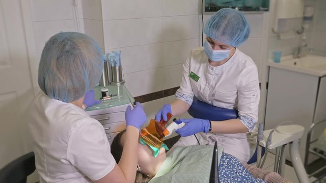 Woman at dentist clinic gets dental treatment to fill a cavity in a tooth. Dental restoration and composite material polymerization with UV light and laser. The doctor works with an assistant.