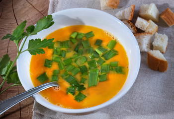 Carrot soup with cream and parsley on dark wooden background Top view. Bread by blocks on a wooden table.