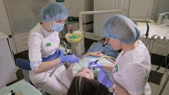 Woman at dentist clinic gets dental treatment to fill a cavity in a tooth. Dental restoration and composite material polymerization with UV light and laser. The doctor works with an assistant.