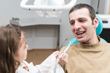 Fototapeta premium Little girl in the role of a dentist prepared to drill teeth to an adult male