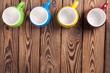 Row of colored empty ceramic clean mugs on old worn brown wooden table. Top view with copy space