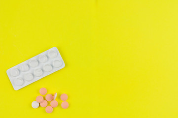 Heap of pills beside used white blister pack on background of yellow paper. Top view