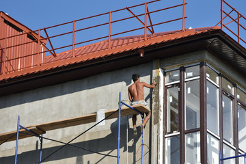 The man builder smears the putty on the wall at a dangerous height