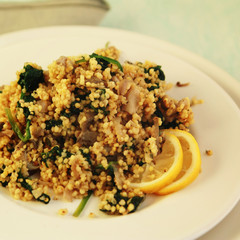Millet with mushrooms and spinach. Jewish cuisine. Vegetarian couscous on the round white plate. Close up. Toned photo.