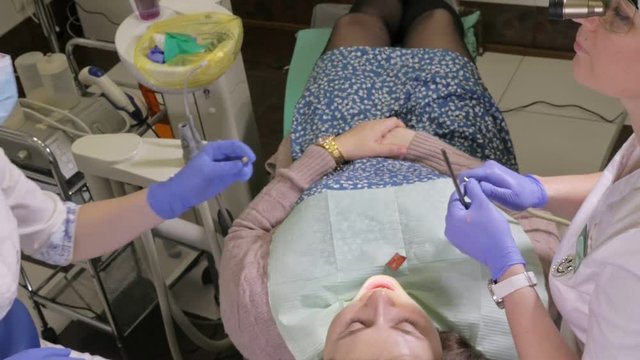 Woman at dentist clinic gets dental treatment to fill a cavity in a tooth. Dental restoration and composite material polymerization with UV light and laser. The doctor works with an assistant.