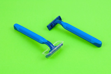 Two new blue plastic disposable razors with two blades and humid strip in transparent cover on blank green paper
