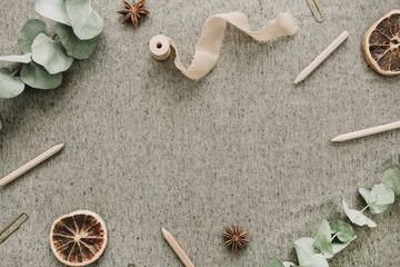 Frame of eucalyptus branches, pencils, dry oranges on beige blanket background. Flat lay, top view rustic mock up with space for text.