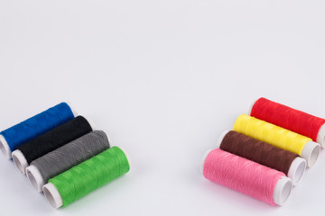 Two rows of bobbins of new colorful threads on white background