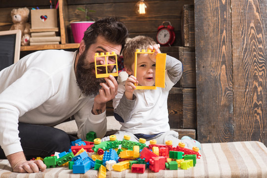 Family fun time. Happy dad and son look through small plastic window and door. Father and blond kid play with colorful plastic blocks on sofa