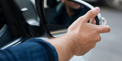 The panorama of young human hand is preparing or correct car mirror for the trip or travel from car window.