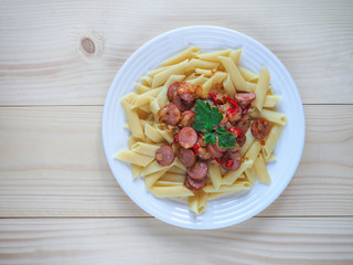 Pasta with fried sausages on rough wooden background. Simple village food.
