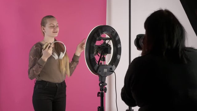 Stock photographer taking pictures in studio. Young model as vlogger recording video blog. Backstage shot during photoshoot