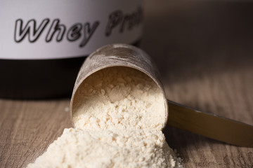 Whey Protein. Golden scoop on wooden background with vanilla powder flavour. Black jar behind