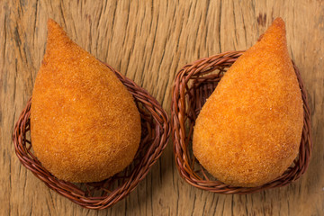 Coxinha is a deep fried food, traditional in Brazil. Two snacks in basket on rustic wood, flat lay.
