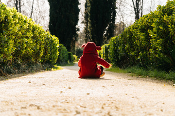 a little kid, a child, in a ridiculous suit sits in a park on the ground and studies the world