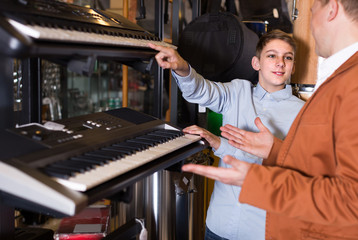 Teenage boy and father choosing best keyboard in musical shop