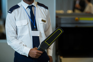 Airport security officer holding metal detector in airport terminal