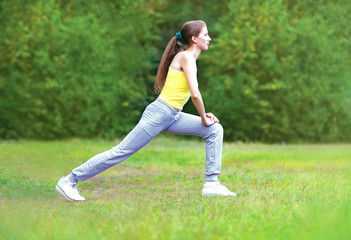 Sport, fitness, yoga concept - young woman is doing stretching exercises on the grass in the park